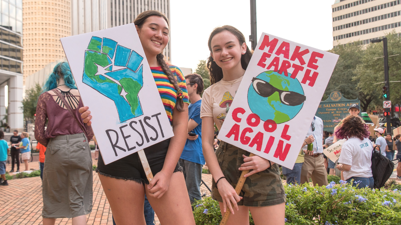 Two young women hold climate justice signs and smile